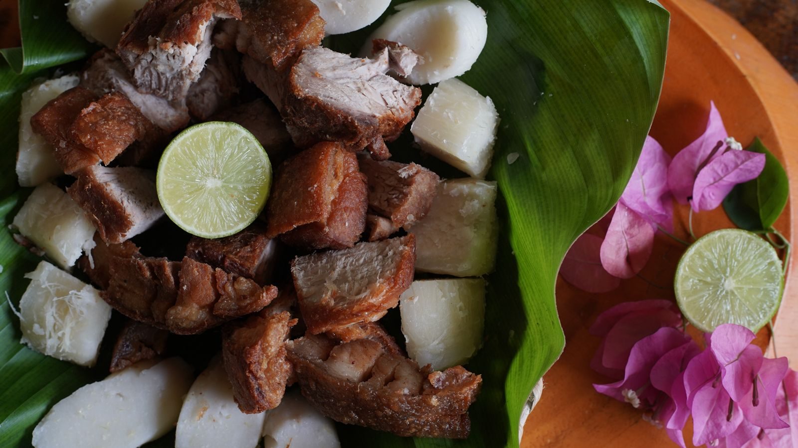 Chicharrón y yuca sobre hoja de plátano, con limón y flores de buganvilla